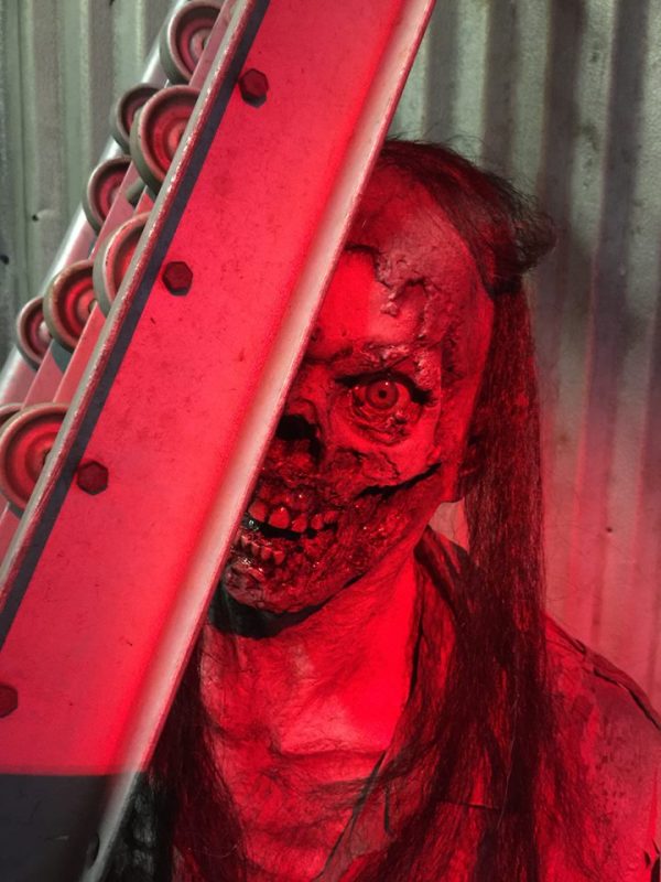 A zombie's face peeking from behind a red metal beam.