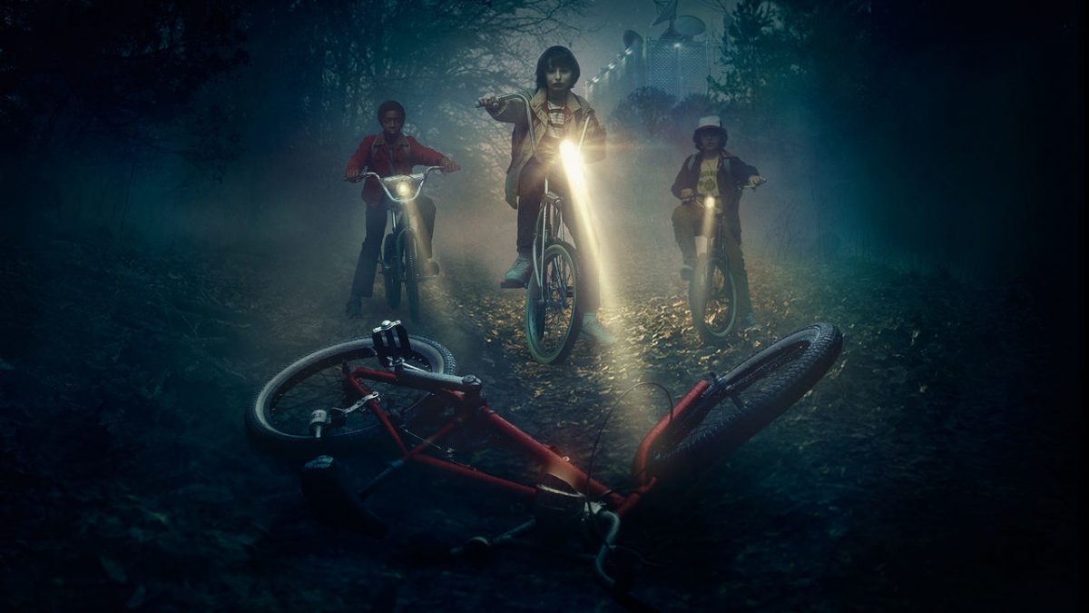 Three kids ride bikes in a dark forest.