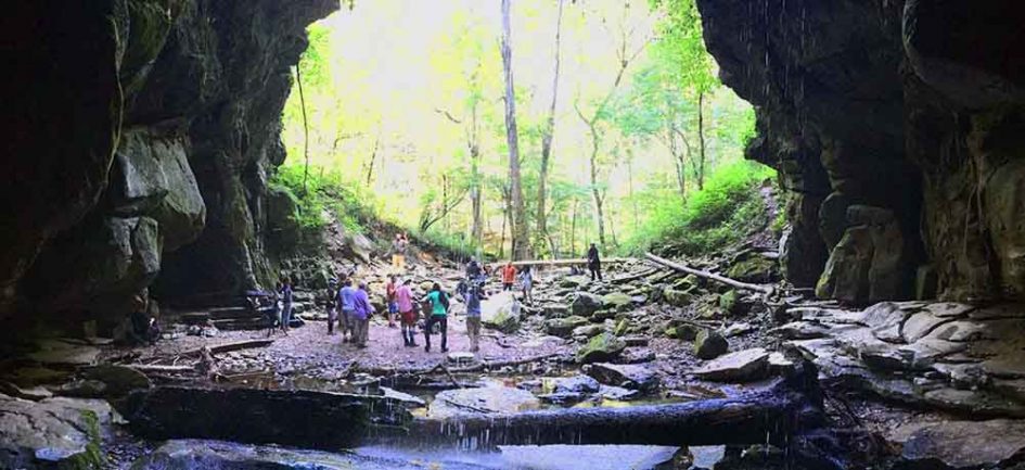 People exploring a cave entrance with a stream.