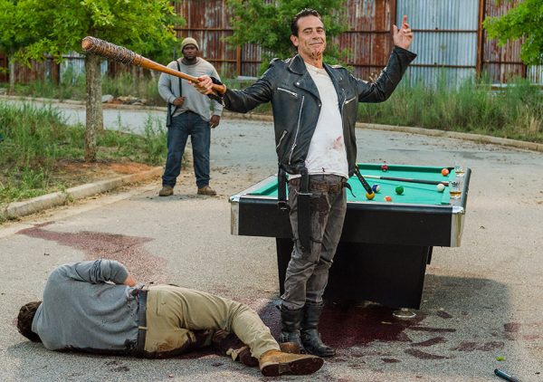 Man holding a bat smiles over a dead body.