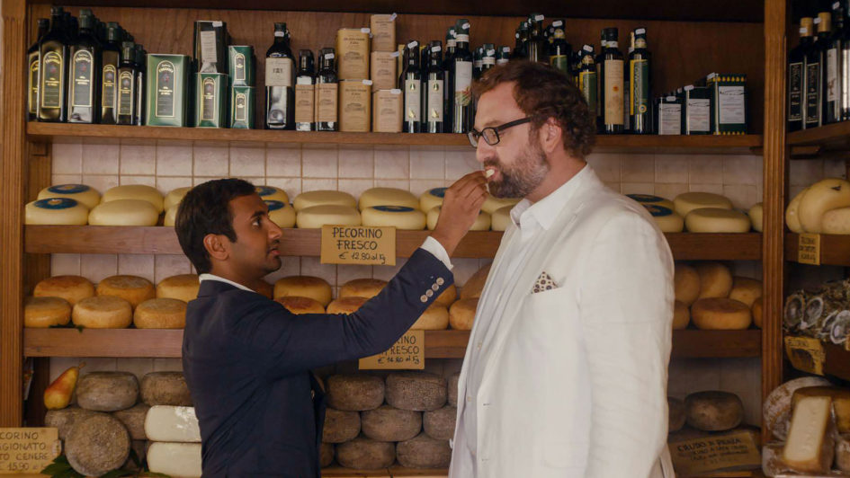 Two men in a cheese shop, one tasting.