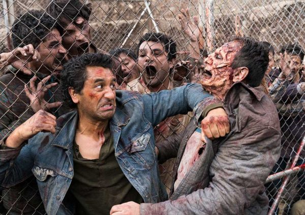 A man fights a zombie behind a fence.