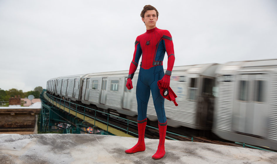 Spider-Man stands on a platform with a train passing by.