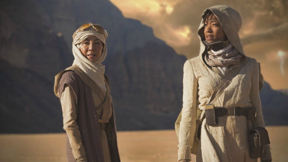 Two women in desert garb stand in a desert.