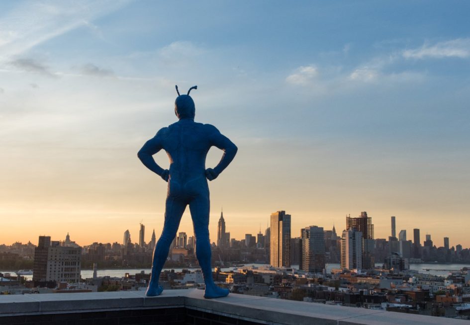 Blue superhero overlooking city skyline.