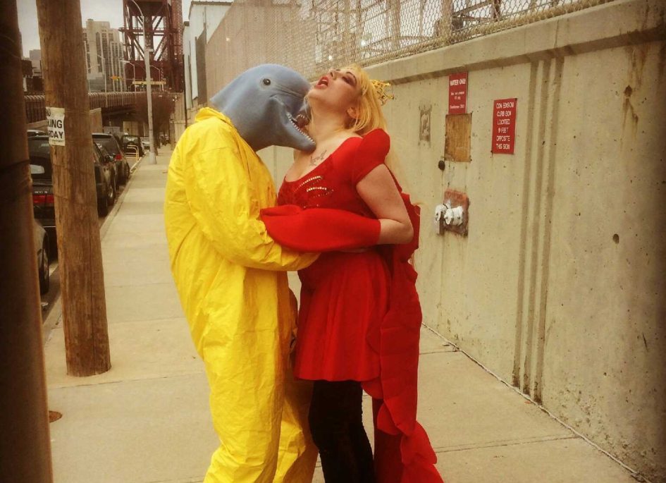 A person in a shark costume hugging a woman in red.