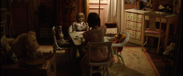 A girl sits at a table with dolls.