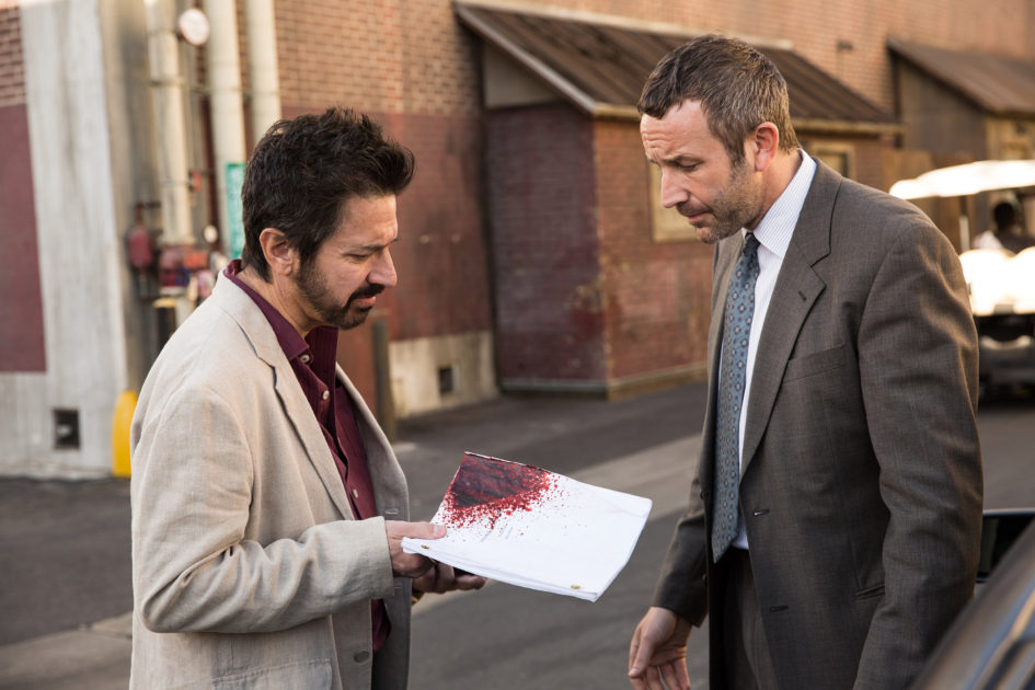 Two men looking at a bloody script.