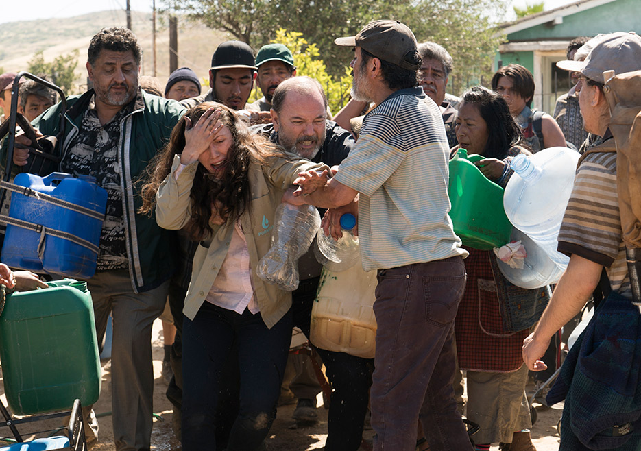 A woman cries while carrying water jugs.