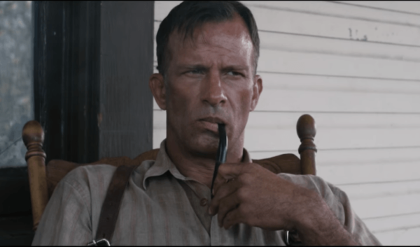 Man holding a pipe, sitting on a porch.