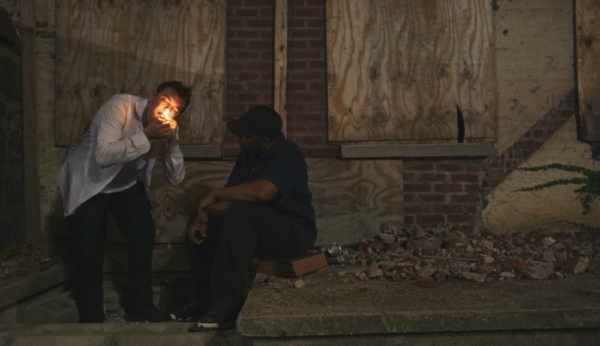 Two men standing by a brick wall.