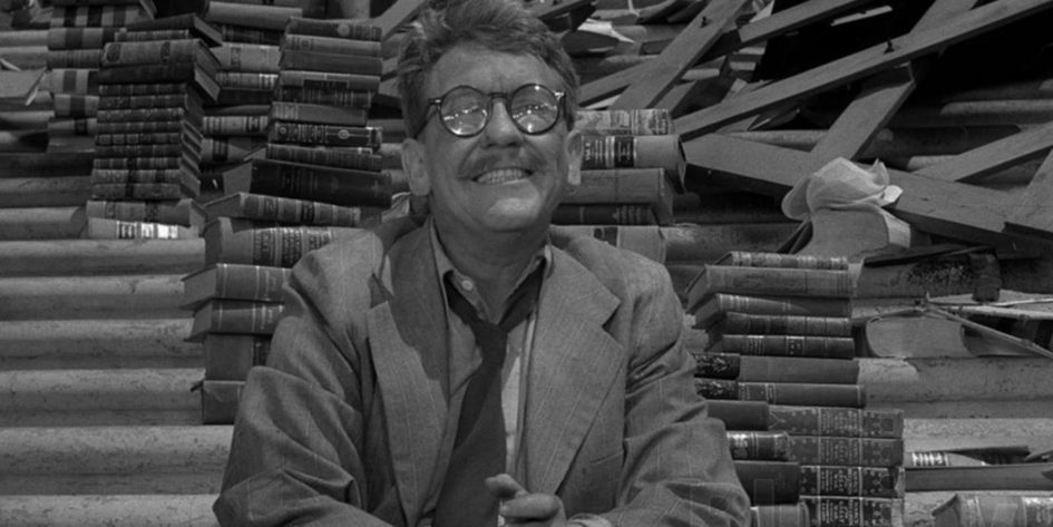 Man smiles surrounded by stacks of books.