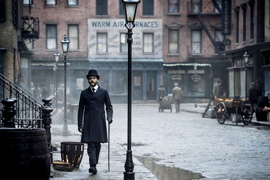 Man in coat walking down a cobblestone street.