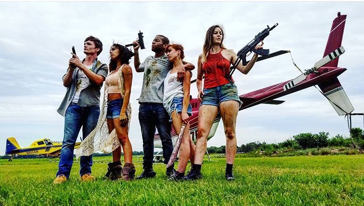 Five people posing with weapons near a helicopter.