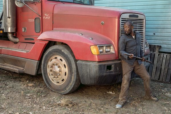 Man with a stick standing by a red truck.