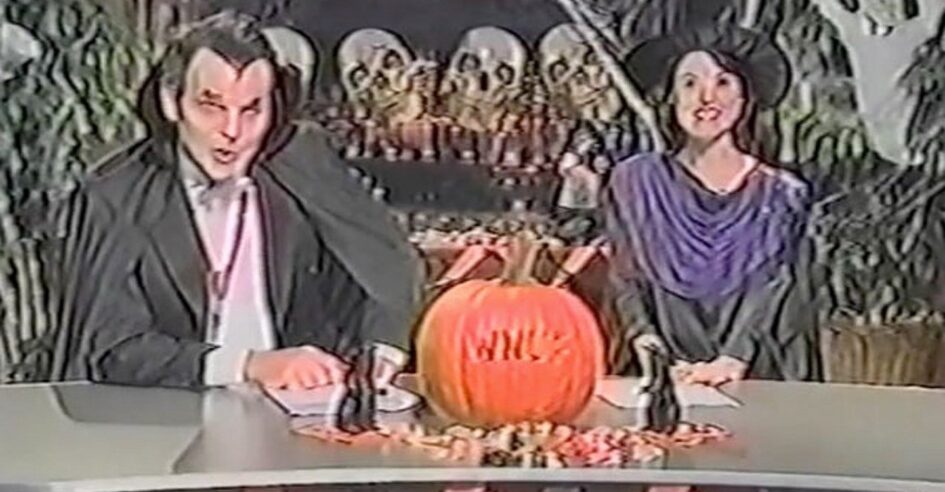 News anchors dressed in Halloween costumes on set with pumpkin