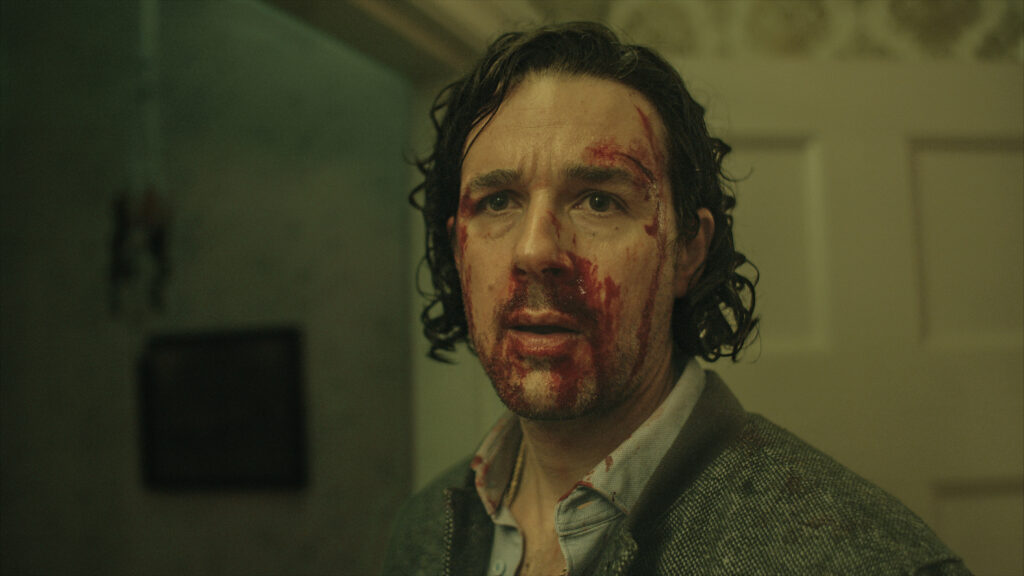 Gino stairs into the camera with blood on his face while fighting the undead in Unholy Night.